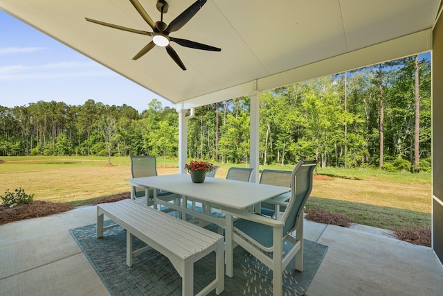 view of patio / terrace with a ceiling fan, outdoor dining space, and a view of trees