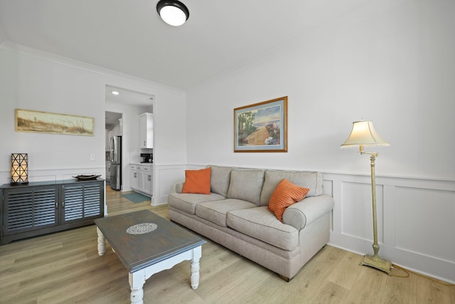 living area with ornamental molding, light wood finished floors, wainscoting, and a decorative wall