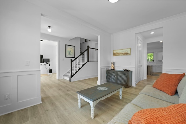 living room with stairway, a decorative wall, light wood-style flooring, a wainscoted wall, and ornamental molding