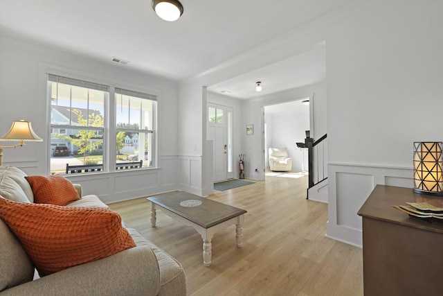 living room with a decorative wall, light wood-style flooring, and wainscoting