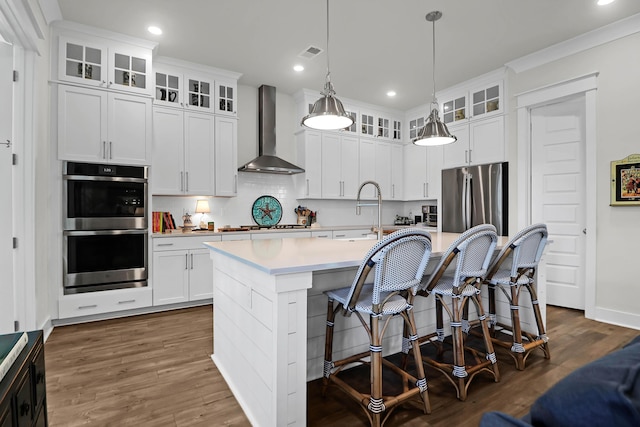 kitchen featuring white cabinetry, hanging light fixtures, a kitchen breakfast bar, a kitchen island with sink, and wall chimney range hood