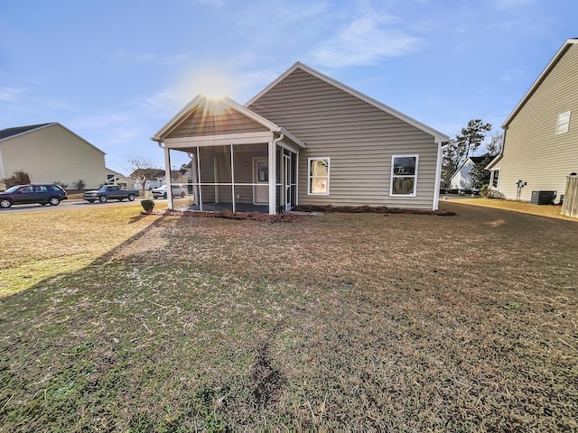 rear view of property with central air condition unit, a sunroom, and a lawn