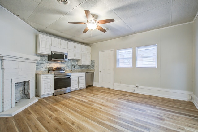 kitchen featuring tasteful backsplash, appliances with stainless steel finishes, a fireplace, white cabinets, and light wood-type flooring