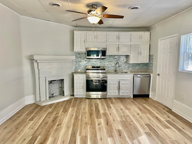 kitchen with appliances with stainless steel finishes, white cabinetry, ornamental molding, and sink