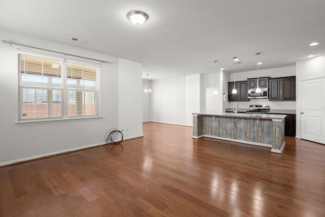 kitchen with an island with sink, dark wood-style floors, appliances with stainless steel finishes, light countertops, and hanging light fixtures