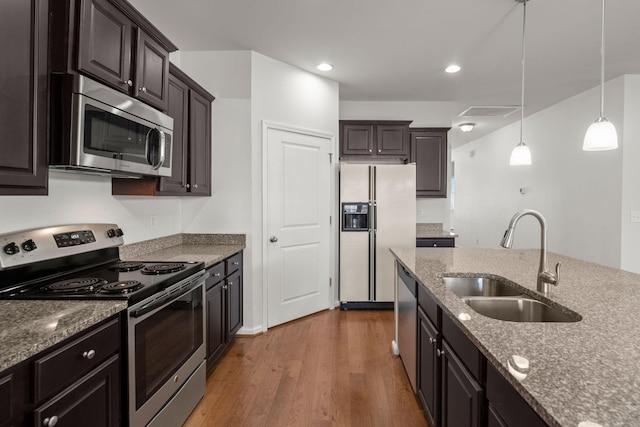 kitchen with wood finished floors, stone countertops, a sink, hanging light fixtures, and appliances with stainless steel finishes