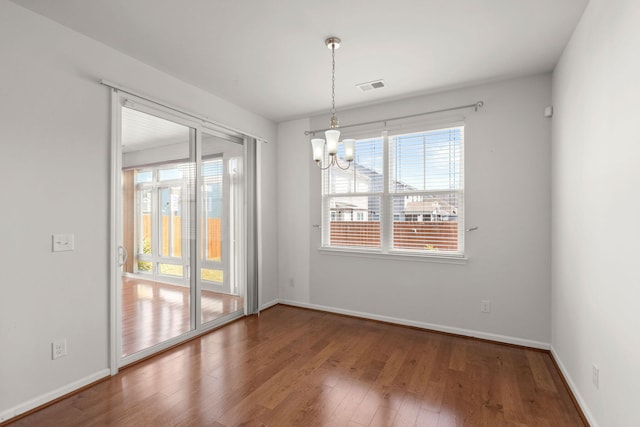 unfurnished dining area with baseboards, visible vents, wood-type flooring, and an inviting chandelier