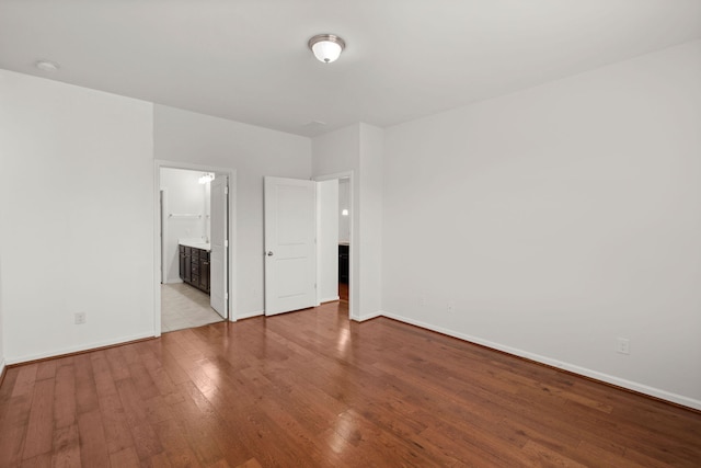 unfurnished bedroom with connected bathroom, baseboards, and hardwood / wood-style flooring