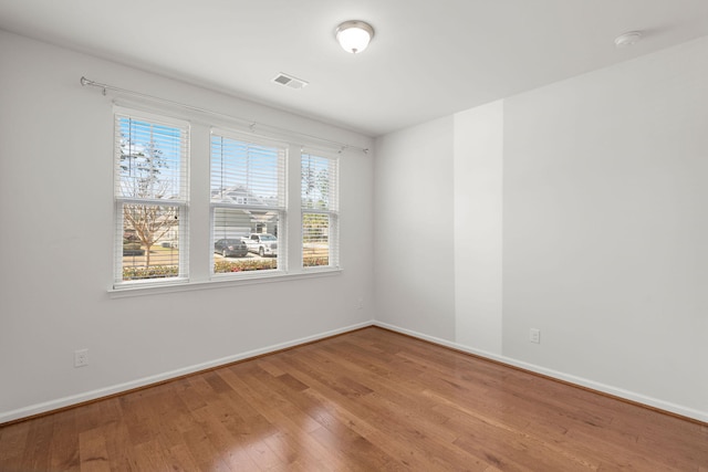 empty room featuring wood finished floors, visible vents, and baseboards