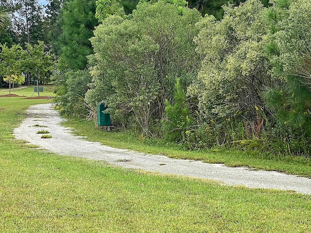 view of home's community with gravel driveway, a lawn, and a wooded view