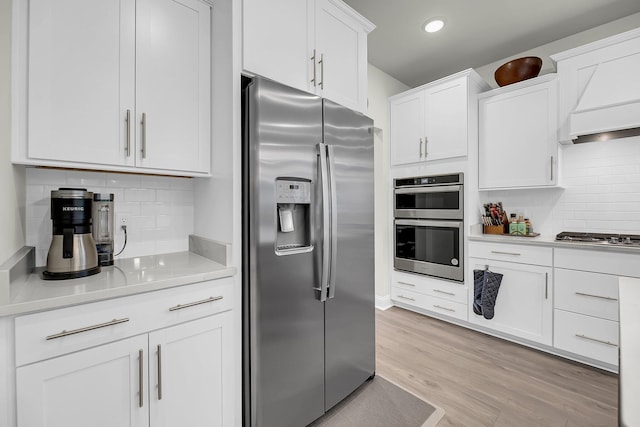 kitchen with decorative backsplash, white cabinets, stainless steel appliances, light countertops, and light wood-type flooring