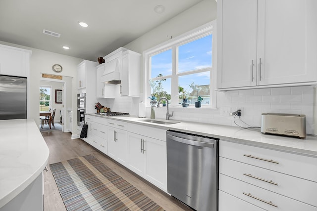 kitchen featuring tasteful backsplash, appliances with stainless steel finishes, light wood-style floors, white cabinetry, and a sink