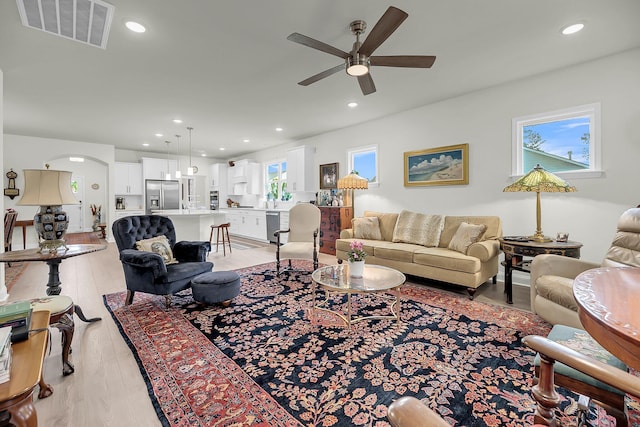 living area featuring arched walkways, light wood-style flooring, recessed lighting, a ceiling fan, and visible vents