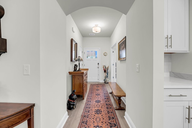 doorway to outside featuring arched walkways, light wood finished floors, visible vents, and baseboards