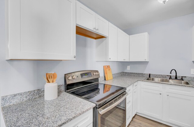 kitchen featuring electric range, sink, white cabinetry, and light hardwood / wood-style floors