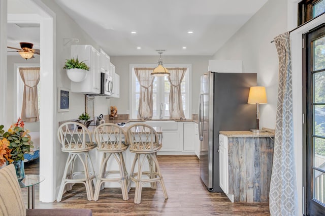 kitchen with light stone countertops, white cabinetry, stainless steel appliances, hardwood / wood-style flooring, and ceiling fan