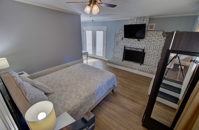 bedroom with a brick fireplace, french doors, hardwood / wood-style flooring, ceiling fan, and crown molding