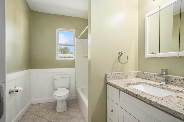 bathroom with toilet, wainscoting, vanity,  shower combination, and tile patterned flooring