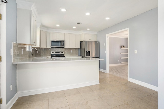 kitchen featuring stainless steel appliances, light countertops, white cabinets, a sink, and a peninsula