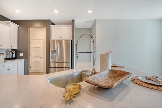 kitchen with recessed lighting, a sink, white cabinets, stainless steel fridge with ice dispenser, and light stone countertops