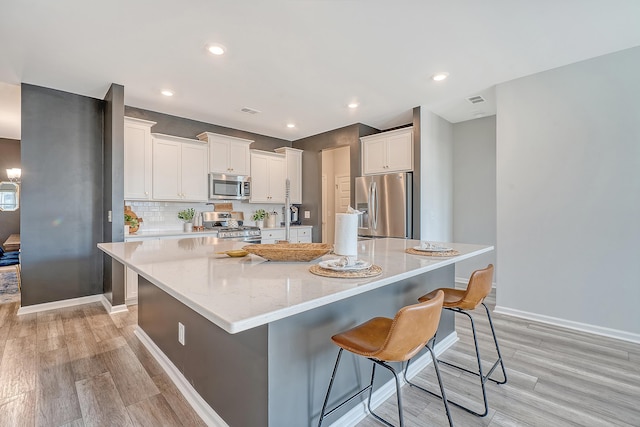 kitchen featuring a large island, light wood-style flooring, decorative backsplash, appliances with stainless steel finishes, and white cabinetry