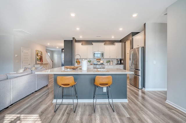 kitchen featuring a breakfast bar, stainless steel appliances, light wood-style floors, open floor plan, and white cabinetry