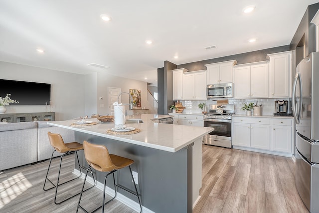 kitchen featuring appliances with stainless steel finishes, a sink, light wood-style floors, white cabinetry, and backsplash