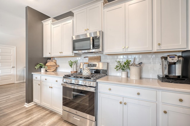 kitchen featuring stainless steel appliances, white cabinets, light wood-style flooring, and tasteful backsplash