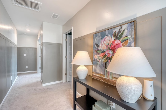 corridor with light carpet, wainscoting, visible vents, and a decorative wall