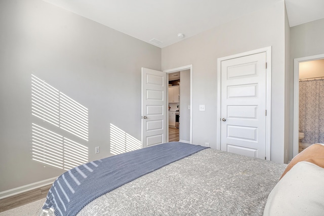 bedroom featuring visible vents, baseboards, wood finished floors, and ensuite bathroom