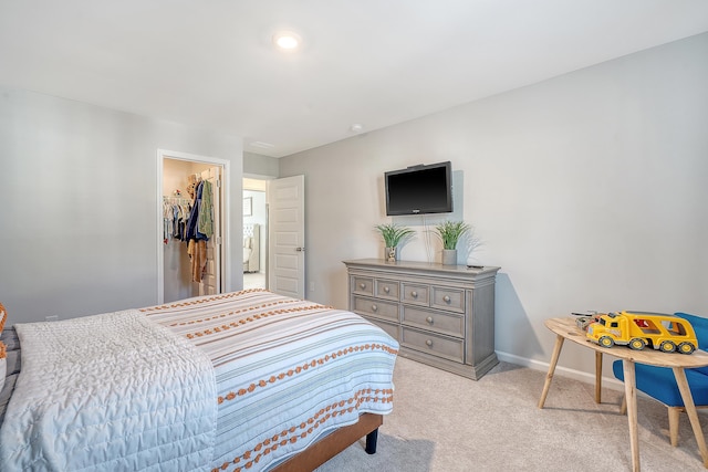 carpeted bedroom featuring a closet, a walk in closet, and baseboards