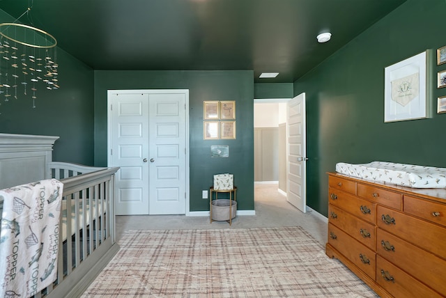 bedroom featuring a closet, light carpet, a crib, and baseboards