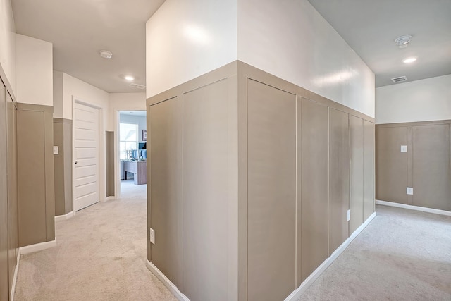 corridor with a decorative wall, visible vents, and light colored carpet