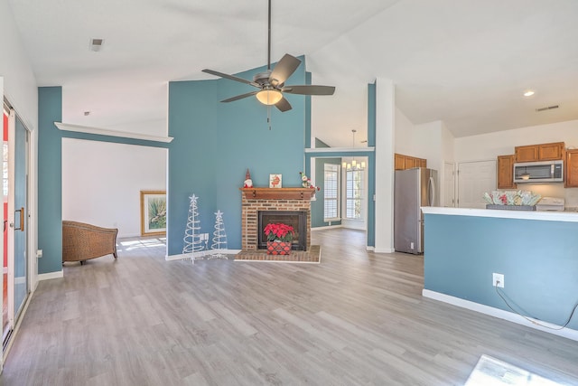 unfurnished living room with a fireplace, high vaulted ceiling, ceiling fan, and light wood-type flooring