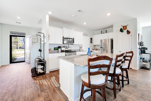 kitchen featuring light stone countertops, light wood-type flooring, an island with sink, white cabinetry, and stainless steel appliances