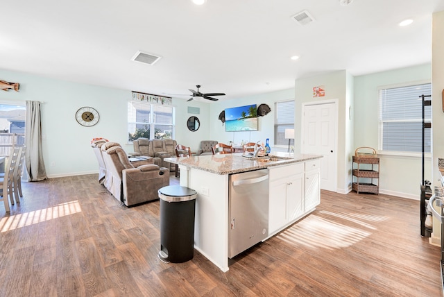 kitchen with light wood-type flooring, stainless steel dishwasher, a kitchen island with sink, ceiling fan, and white cabinetry