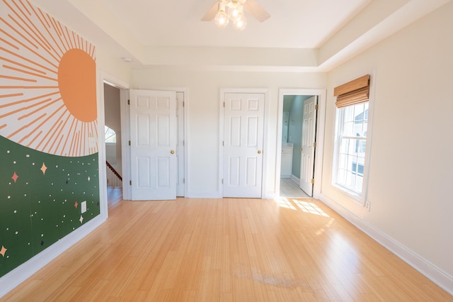 unfurnished bedroom featuring baseboards, wood finished floors, and a tray ceiling