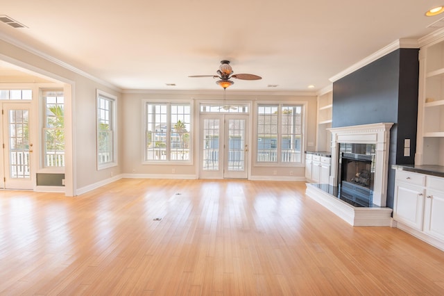 unfurnished living room featuring crown molding, a fireplace with raised hearth, a ceiling fan, light wood-type flooring, and visible vents