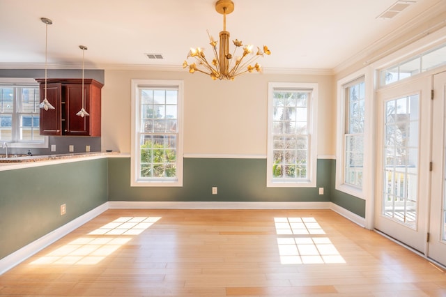 unfurnished dining area featuring crown molding, light wood-style floors, a notable chandelier, and visible vents