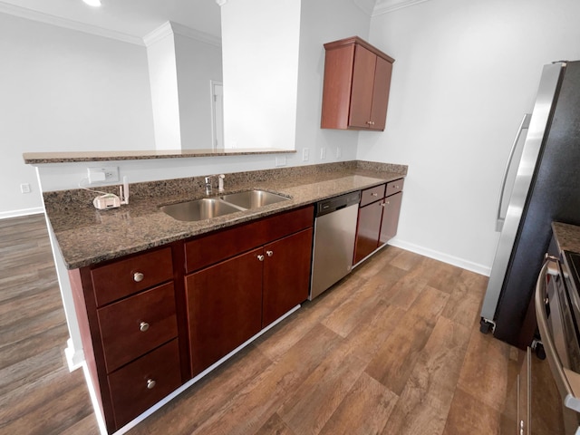 kitchen featuring dark wood-style floors, a peninsula, stainless steel appliances, a sink, and crown molding