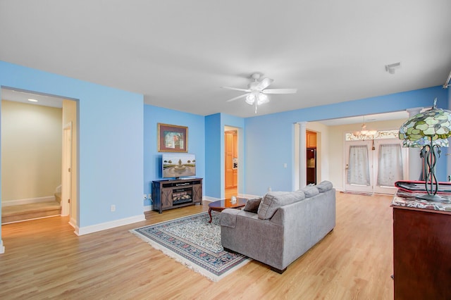 living room featuring light wood-type flooring, ceiling fan with notable chandelier, baseboards, and stairs