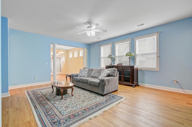 living area with visible vents, baseboards, ornate columns, wood finished floors, and ceiling fan with notable chandelier