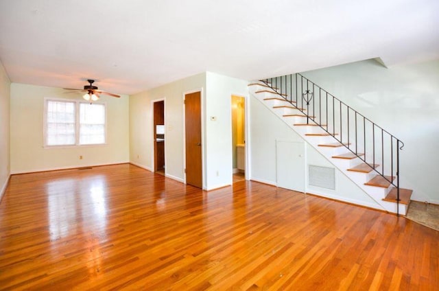 unfurnished living room with a ceiling fan, stairway, wood finished floors, and visible vents