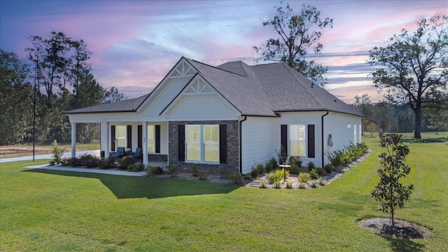back of property with a yard, stone siding, and a shingled roof