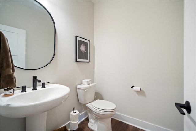 half bath with baseboards, wood finished floors, toilet, and a sink