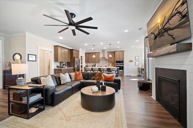 living area featuring ceiling fan, ornamental molding, recessed lighting, dark wood-style floors, and a glass covered fireplace