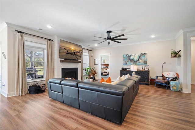 living room with a large fireplace, wood-type flooring, crown molding, and ceiling fan