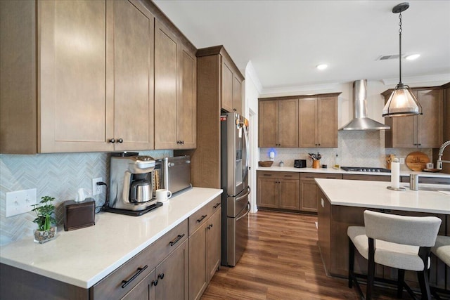 kitchen featuring wall chimney range hood, stainless steel fridge with ice dispenser, decorative backsplash, a kitchen bar, and light countertops