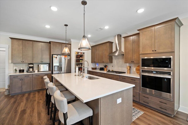 kitchen with appliances with stainless steel finishes, wall chimney exhaust hood, a sink, tasteful backsplash, and dark wood finished floors
