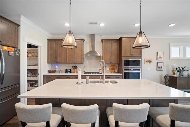 kitchen with appliances with stainless steel finishes, wall chimney range hood, a sink, crown molding, and tasteful backsplash